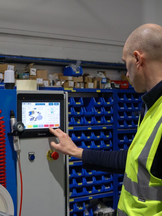 A technician in a hi-vis vest operating a Weintek touchscreen control panel on a Motion Drives and Controls machine in a warehouse.
